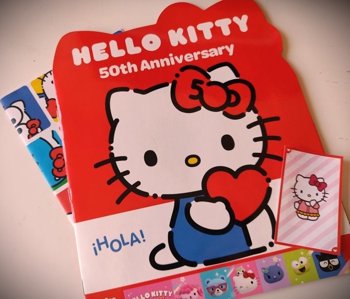 Photo of my Hello Kitty album from the 50th anniversary with the poster and an extra card next to it.